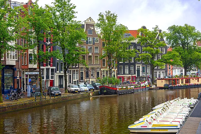 The Prinsengracht canal in Amsterdam, lined with trees and gabled canal houses, with pedal boats moored in the foreground